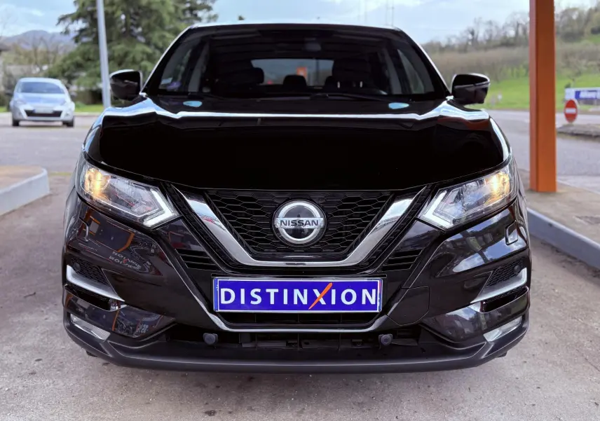 Vue frontale d'un Nissan Qashqai noir avec calandre chromée et phares allumés, plaque Distinxion visible.