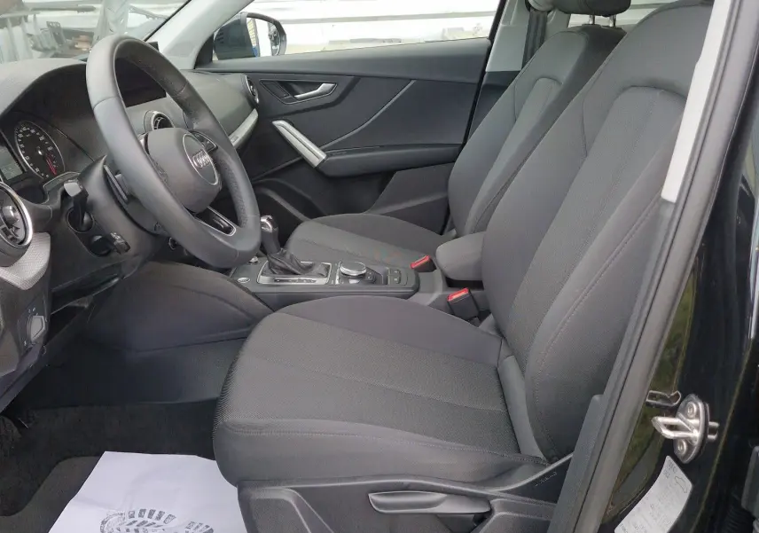 Intérieur côté conducteur d’Audi Q2 noir mito metal 2023, sièges tissu noir et volant multifonction visible.