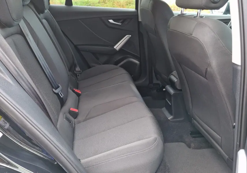 Vue intérieure arrière côté droit de l'Audi Q2 35 TFSI 2023 noir mito metal, sièges tissu noir et ceintures visibles.