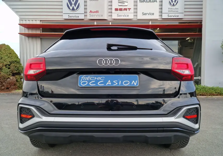 Vue arrière d'un Audi Q2 35 TFSI noir mito metal avec feux rouges et plaque d'occasion bleue visible.