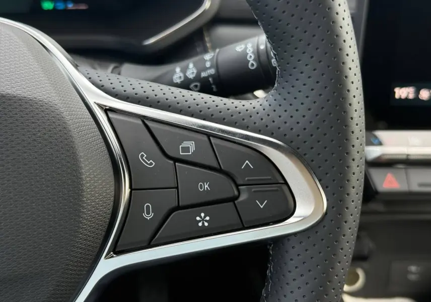Gros plan sur les commandes multifonctions noires du volant perforé côté gauche du Renault Symbioz gris Rafale.