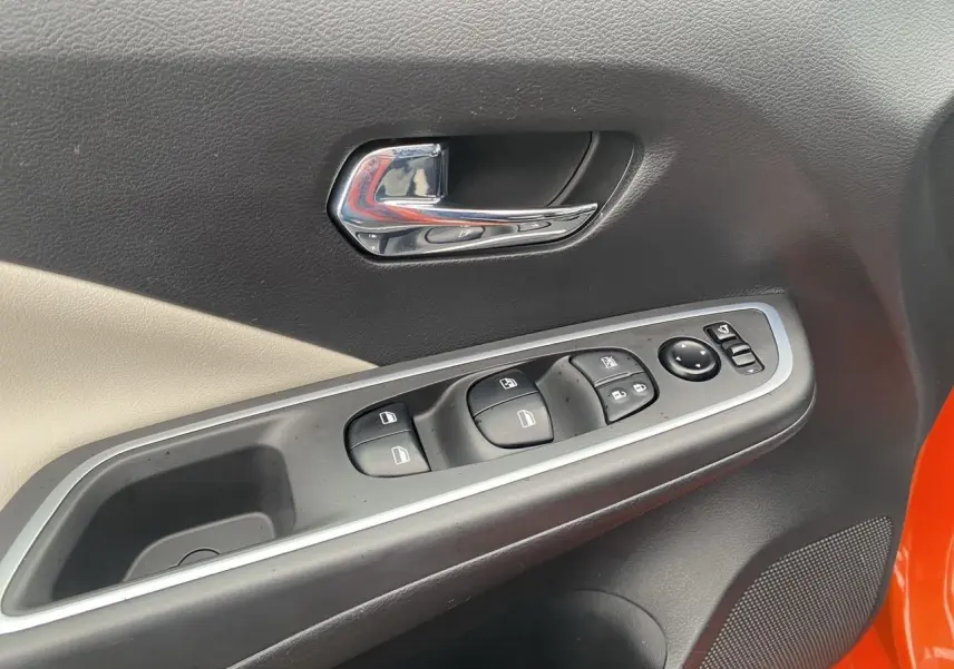 Gros plan sur la porte avant gauche de la Nissan Micra orange Energy, montrant les commandes des vitres et la poignée chromée.