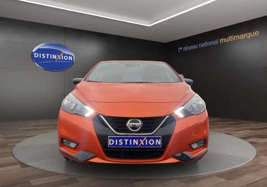 Vue de face d'une Nissan Micra 2022 orange Energy avec phares allumés dans un showroom Distinxion.