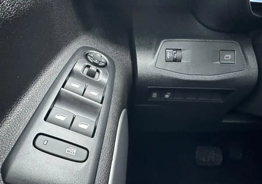 Gros plan sur les commandes de lève-vitres et réglages lumineux côté gauche intérieur du Citroën Berlingo gris Artense 2025.
