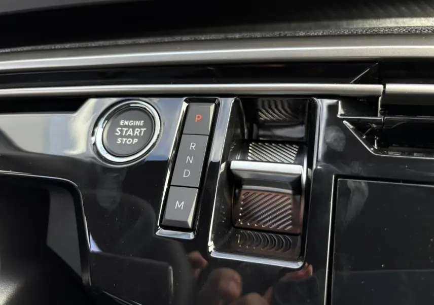 Gros plan sur la console centrale noire brillante du Peugeot 5008 Hybrid avec bouton start/stop et sélecteur de boîte auto.