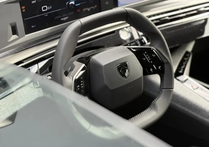 Gros plan sur le volant cuir noir et le tableau de bord numérique du Peugeot 5008 Hybrid 145 e-DSC6 Allure 2025.