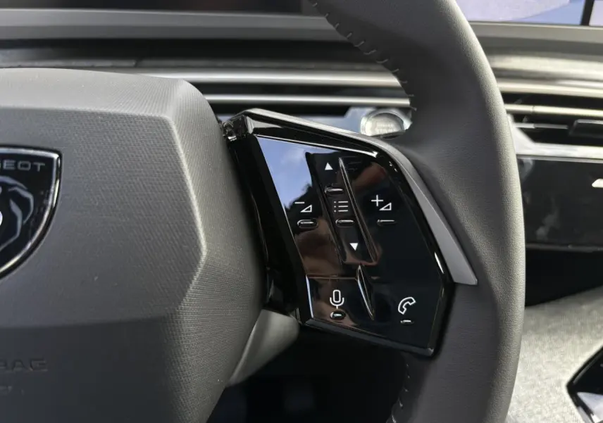 Gros plan sur les commandes noires du volant cuir du Peugeot 5008 Hybrid blanc Okénite, intérieur moderne et épuré.