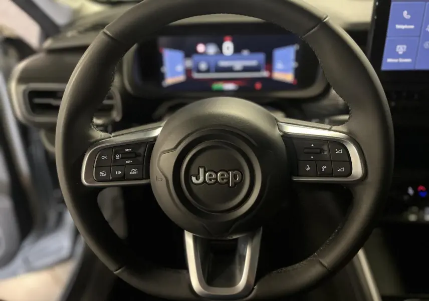 Gros plan sur le volant noir du Jeep Avenger 2024 avec commandes intégrées et tableau de bord numérique flou en arrière-plan.