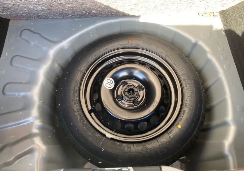 Roue de secours noire dans le coffre d'une Dacia Sandero Stepway 2025, entourée de la carrosserie gris schiste.