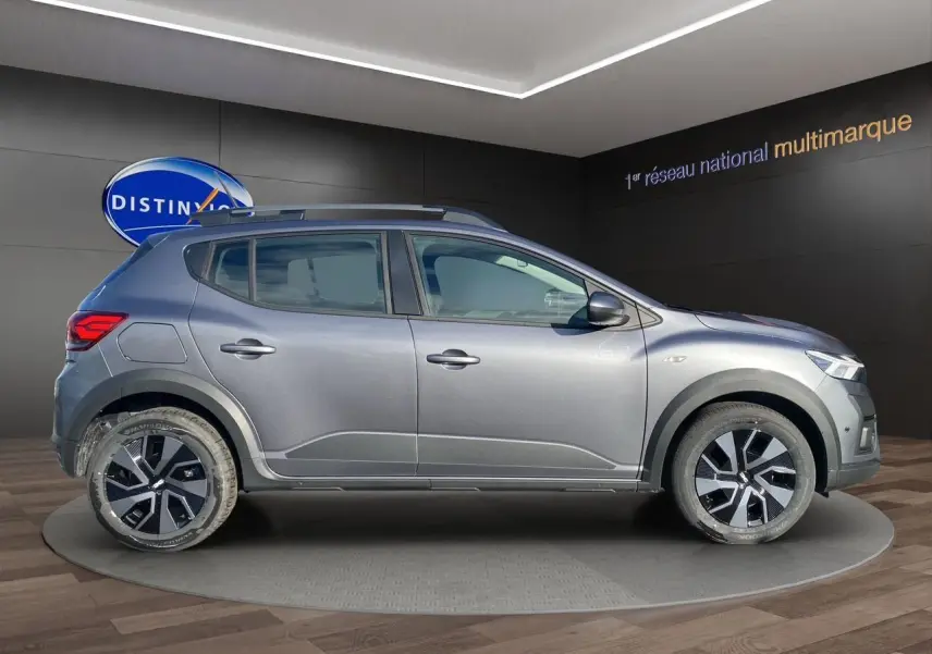 Vue latérale droite d'une Dacia Sandero Stepway gris schiste avec barres de toit et jantes modernes en concession.