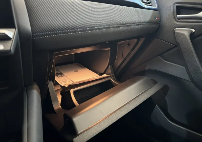 Vue intérieure côté passager du coffre à gants ouvert du Renault Captur blanc esprit Alpine E-Tech 2025 avec documents visibles.