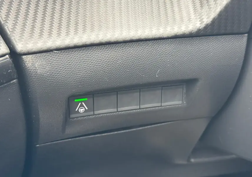 Gros plan sur le tableau de bord noir du Peugeot 208 Hybrid 110, montrant un bouton d’aide au maintien de voie activé.