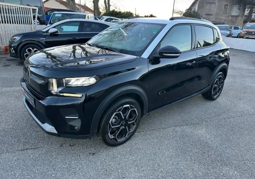 Vue 3/4 avant droite d'une Citroën C3 noire 2025 avec jantes alliage 17 pouces et barres de toit visibles.