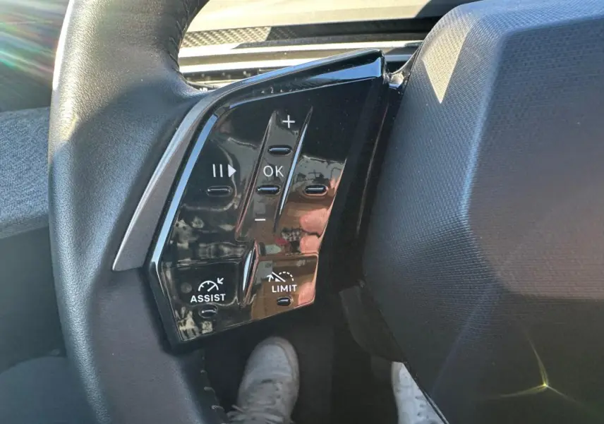 Gros plan sur les commandes à gauche du volant du Peugeot 3008 Hybrid blanc, avec boutons de réglage et assistance.