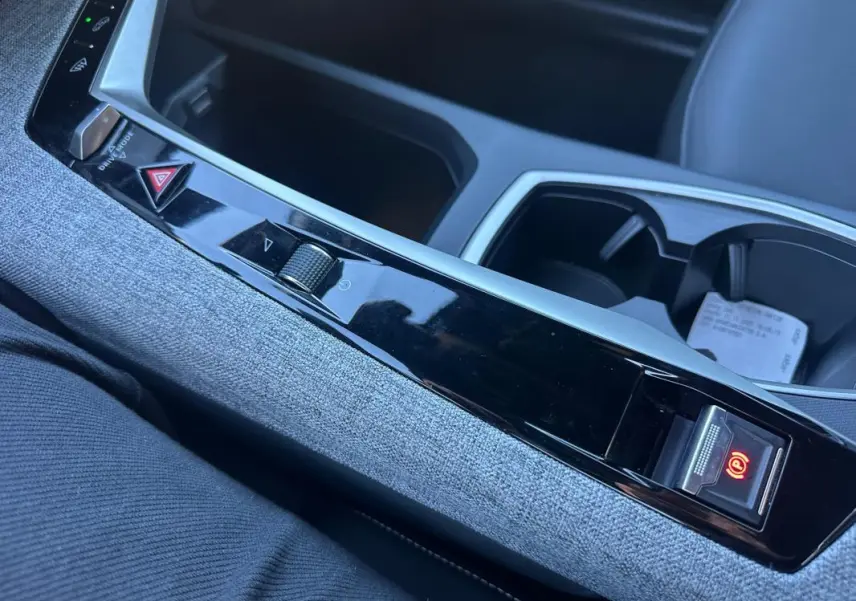 Gros plan sur la console centrale du Peugeot 3008 Hybrid blanc, avec frein à main électrique et habillage tissu gris.