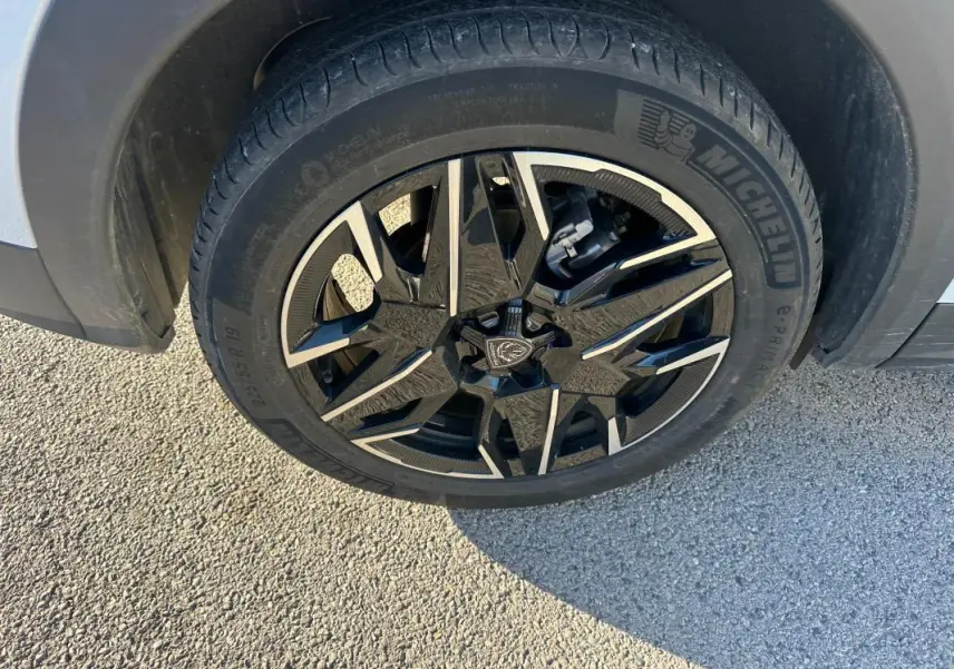 Gros plan sur la jante alliage noire et argent 19 pouces du côté avant droit du Peugeot 3008 blanc Hybrid 145 e-DCS6 Allure.