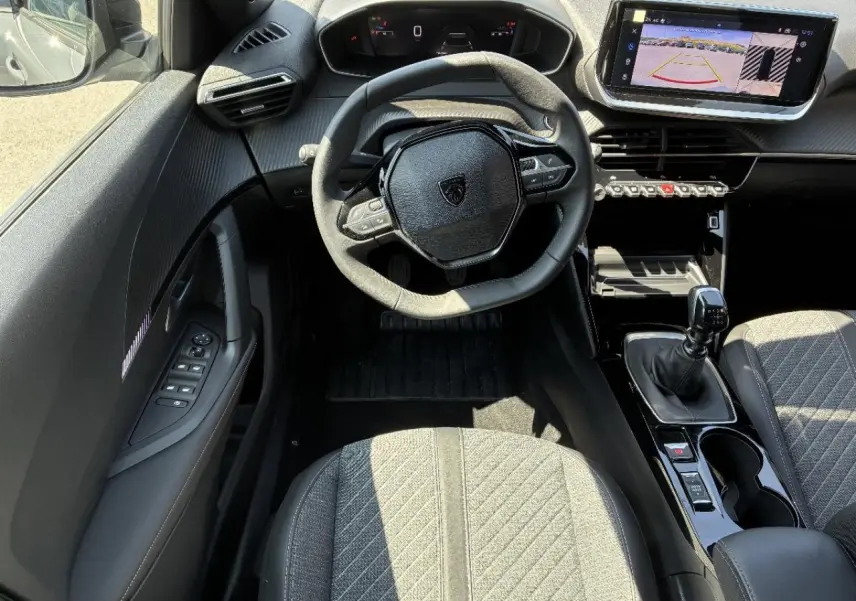 Vue intérieure de face du poste de conduite du Peugeot 2008 1,2 100 CV Allure 2024, volant compact et écran tactile avec caméra de recul.