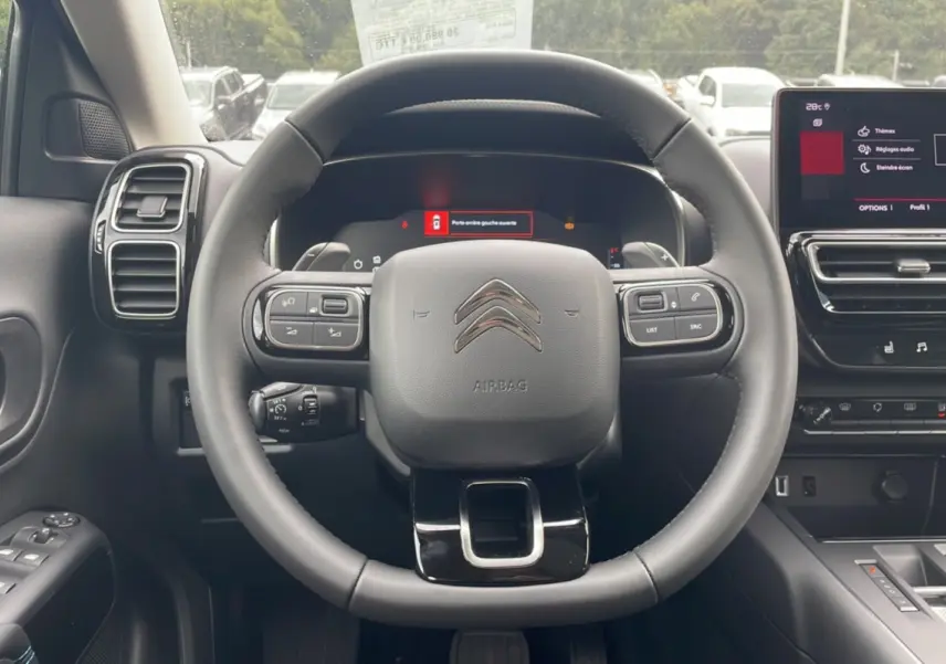 Vue intérieure centrée sur le volant du Citroën C5 Aircross Hybrid 2025 avec tableau de bord numérique et écran tactile.