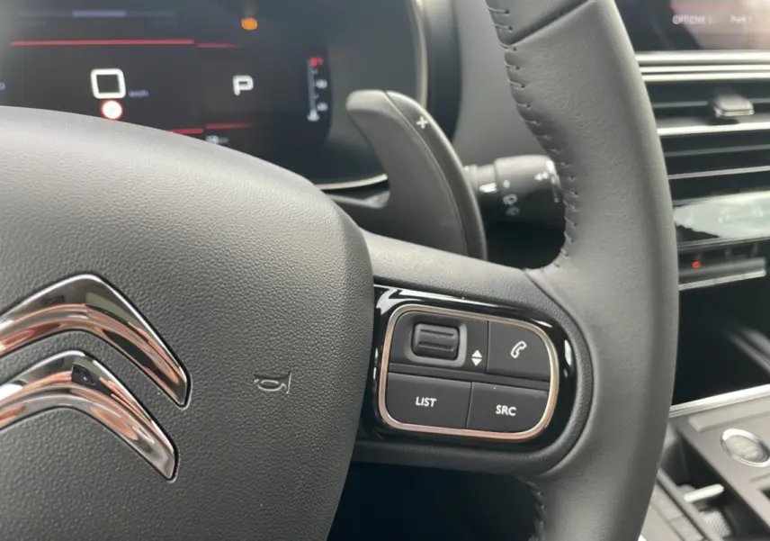 Gros plan sur le volant en cuir du Citroën C5 Aircross Hybrid 2025, avec commandes intégrées et tableau de bord numérique.