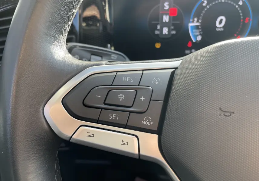 Gros plan sur les commandes de régulateur de vitesse au volant cuir noir du Volkswagen Tiguan 2024, intérieur gris-noir.