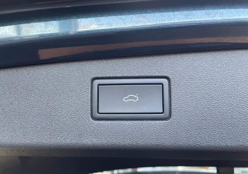 Gros plan sur le bouton d'ouverture électrique du coffre, entouré de plastique noir texturé, sur un Volkswagen Tiguan bleu Nightshade.
