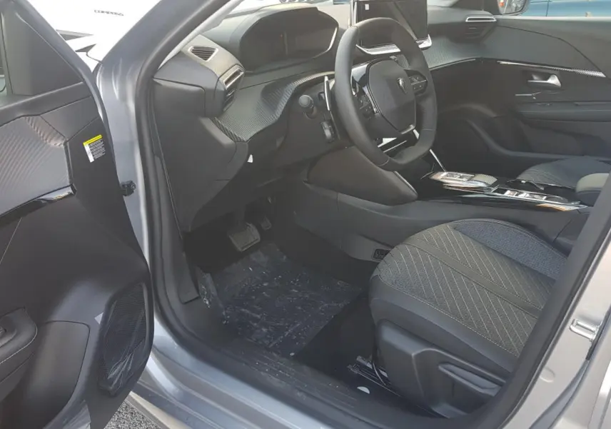 Intérieur côté conducteur de la Peugeot 208 Hybrid gris 2025, avec volant compact et tableau de bord moderne.
