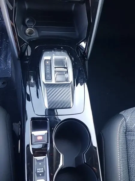 Vue plongeante sur la console centrale noire brillante de la Peugeot 208 Hybrid 110, avec levier de boîte auto et porte-gobelets.