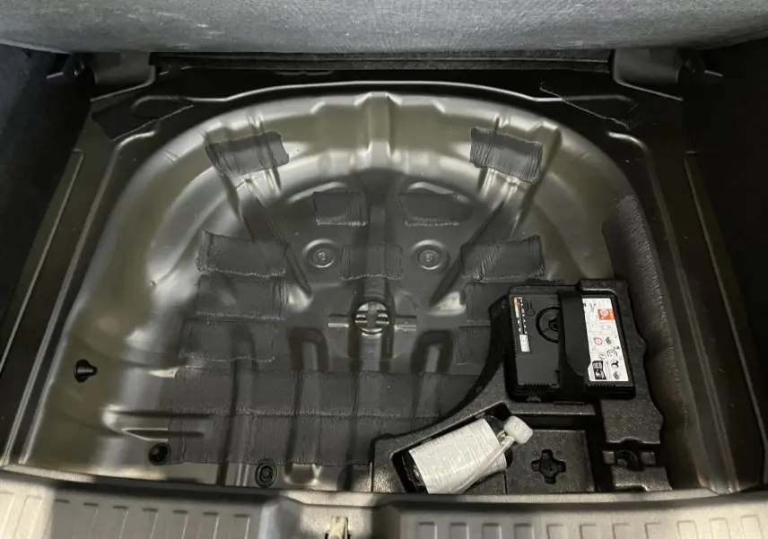 Coffre ouvert en vue plongeante montrant le rangement sous plancher vide avec kit de réparation sur Audi A3 Sportback gris.