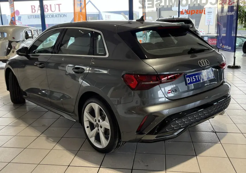 Audi A3 Sportback gris métallisé vue 3/4 arrière droit en intérieur avec jantes alliage et toit ouvrant panoramique.