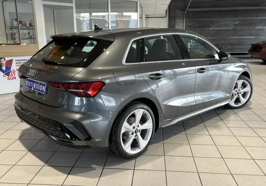 Audi A3 Sportback gris métallisé vue 3/4 arrière droit en intérieur avec jantes 5 branches et toit ouvrant panoramique.