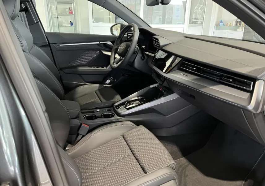 Intérieur noir de l'Audi A3 Sportback 2025 vu côté passager, avec tableau de bord moderne et volant cuir sport.