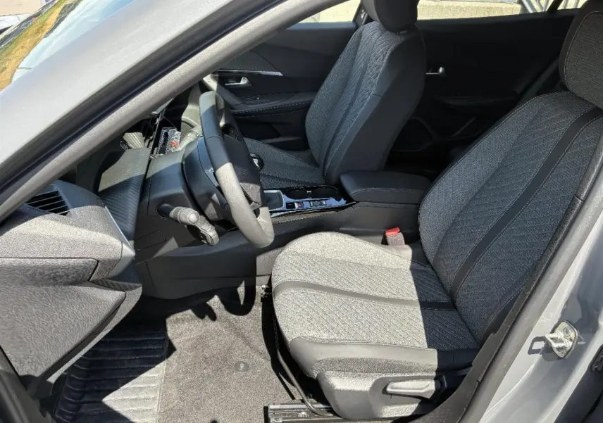 Vue intérieure côté conducteur du Peugeot 2008 1,2 100 CV Allure 2024, sièges tissu gris avec surpiqûres et volant compact.