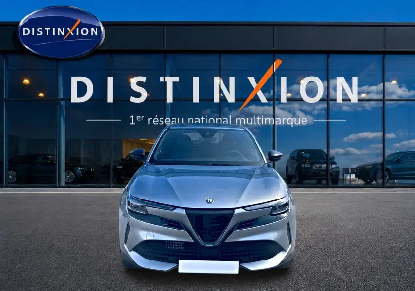 Vue frontale d'une Alfa Romeo Junior 1.2 hybride gris, avec calandre caractéristique et phares LED matrix, devant un showroom.
