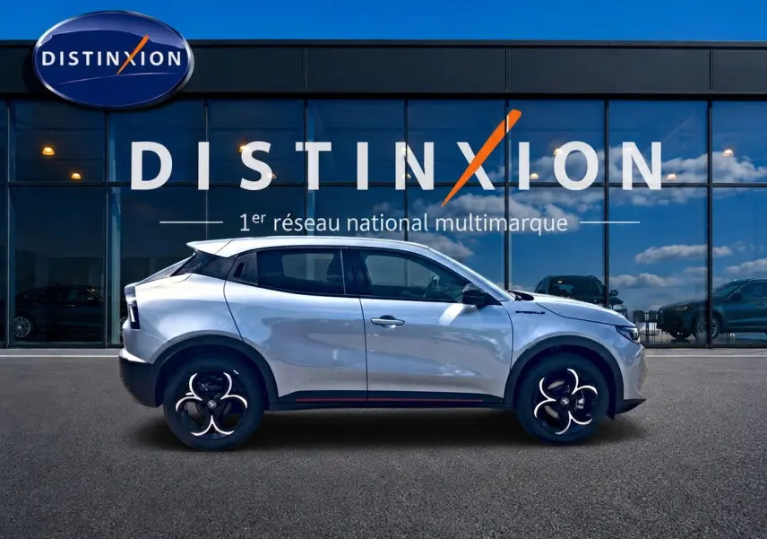 Profil droit de l'Alfa Romeo Junior gris 2026, avec jantes en alliage et vitres teintées, devant une vitrine Distinxion.