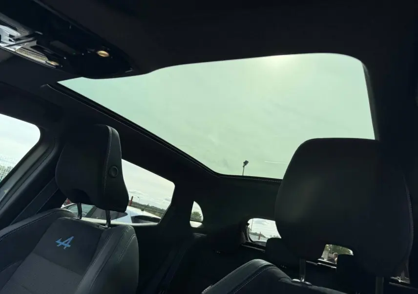 Vue intérieure du toit panoramique et des sièges avant noirs avec logo Alpine bleu sur Renault Austral 2026 gris satin.