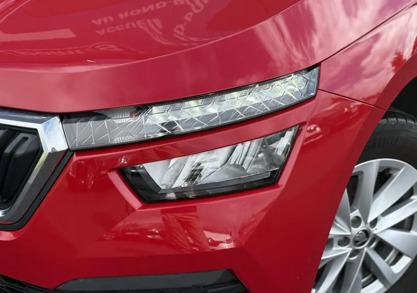 Gros plan sur le phare avant droit et la calandre d'un Skoda Kamiq Rouge Velvet 2024 avec jante alliage.