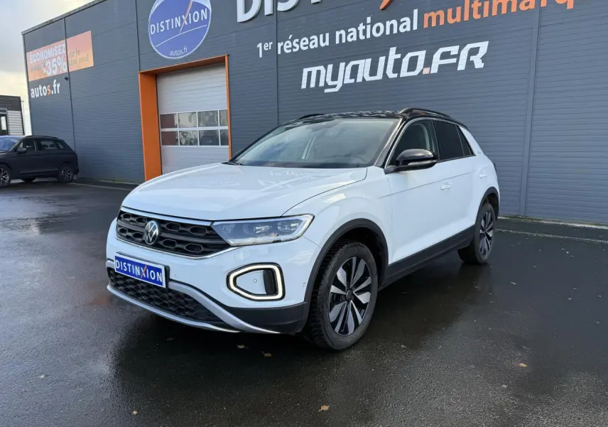 Volkswagen T-Roc blanc pur en 3/4 avant droit avec toit noir et jantes alliage 'Zürich' sur parking humide.