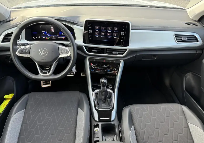 Intérieur du Volkswagen T-Roc 2025 vu de face, avec tableau de bord digital et sièges tissu noir et gris.