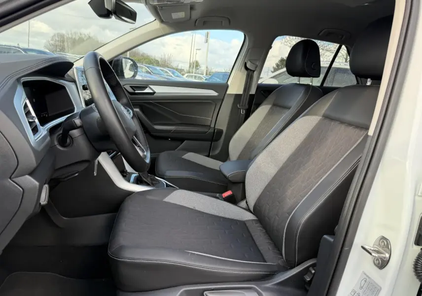 Intérieur côté conducteur du Volkswagen T-Roc blanc pur 2025, sièges bi-matière avec pack confort et volant cuir multifonction.
