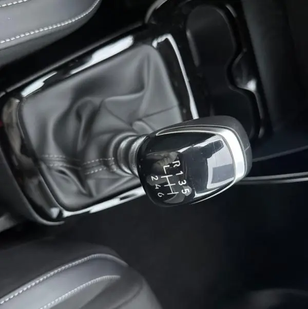 Gros plan sur le levier de vitesses manuel noir de la Citroën C3 gris, entouré de sellerie noire avec surpiqûres blanches.