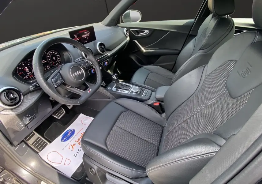 Vue intérieure côté conducteur de l'Audi Q2 35 TDI S-Line 2024 avec sièges cuir noir et volant sport multifonction.