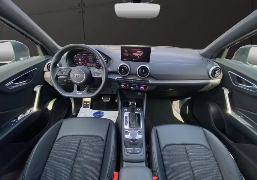 Vue intérieure de l'Audi Q2 35 TDI S-Line 2024, montrant le tableau de bord et les sièges en cuir noir.
