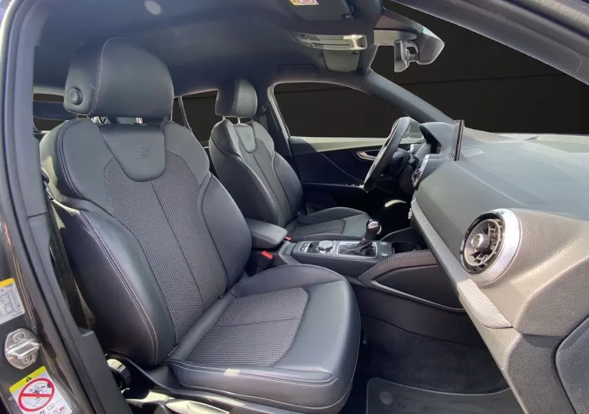 Vue intérieure côté conducteur de l'Audi Q2 S line 2024 avec sièges sport cuir et tableau de bord moderne.
