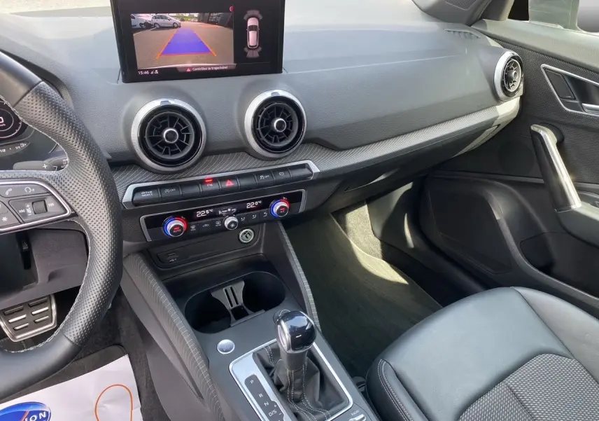 Vue intérieure de l'Audi Q2 35 TDI S-Line montrant le tableau de bord, la caméra de recul à l'écran et la console centrale noire.