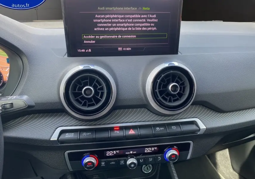 Tableau de bord de l'Audi Q2 35 TDI S-Line 2024 avec écran central et aérateurs ronds en vue frontale rapprochée.