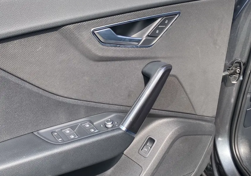 Gros plan sur la porte avant droite de l'Audi Q2 gris Daytona, montrant les commandes de vitres et la poignée intérieure noire.