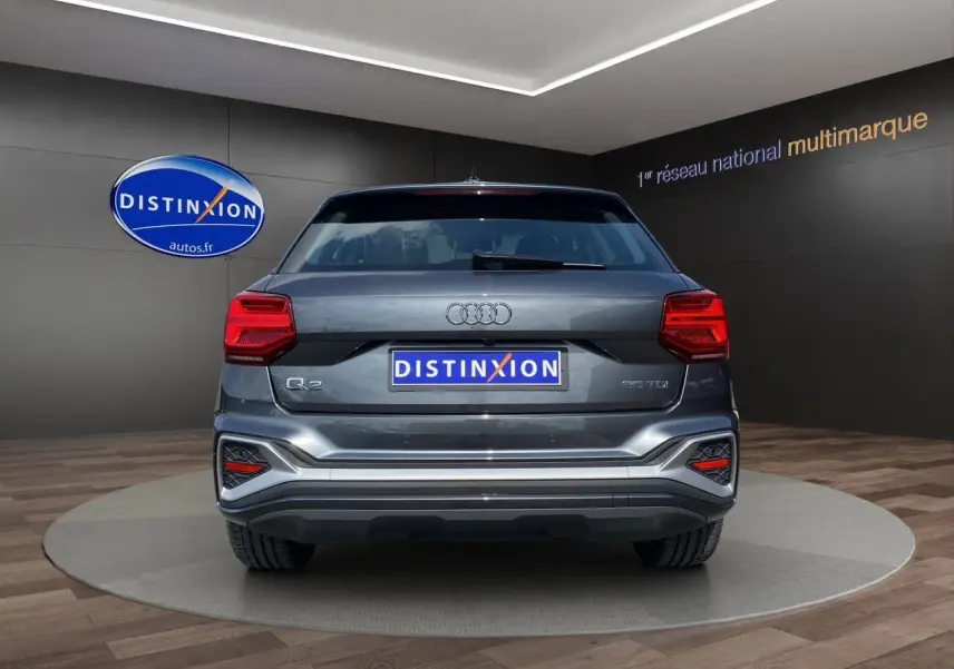 Vue arrière d'un Audi Q2 gris Daytona avec feux LED et logo S line visible sur un podium intérieur.