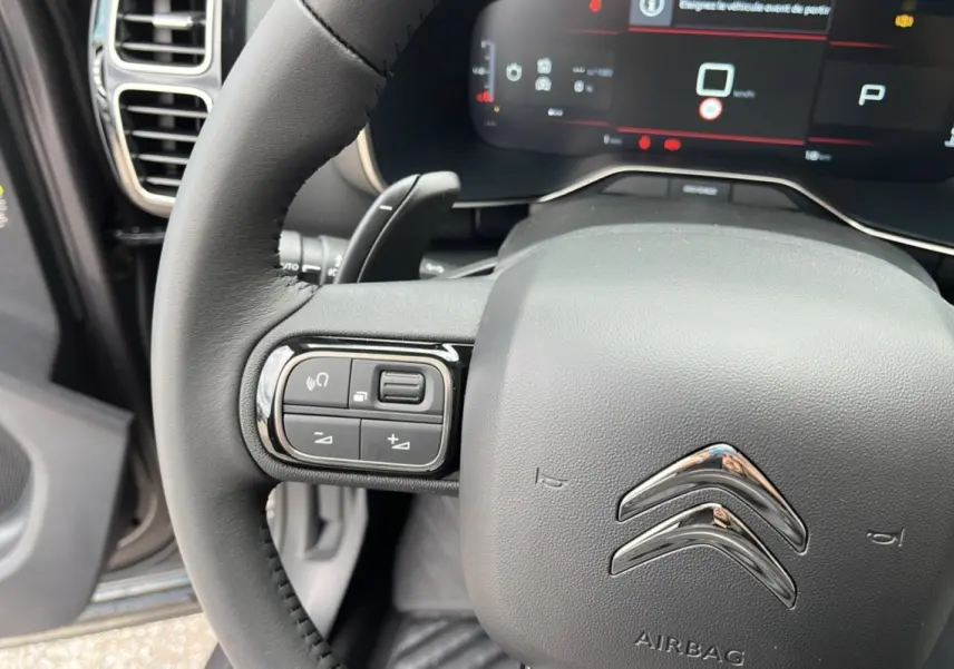 Gros plan sur le volant noir du Citroën C5 Aircross Hybrid 2025 avec commandes intégrées et tableau de bord numérique.