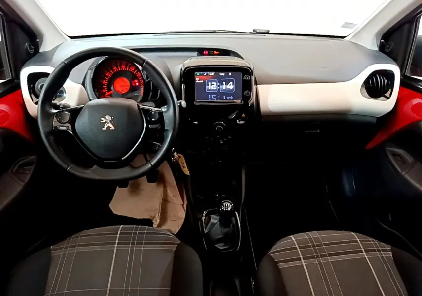 Intérieur avant d'une Peugeot 108 rouge, volant cuir multifonctions, tableau de bord avec écran tactile et sièges à motifs carreaux.