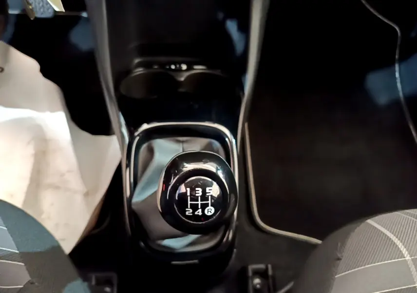 Le levier de vitesses manuel noir de la Peugeot 108 1.0 VTI 68 TOP! STYLE vu de dessus entre les sièges avant.